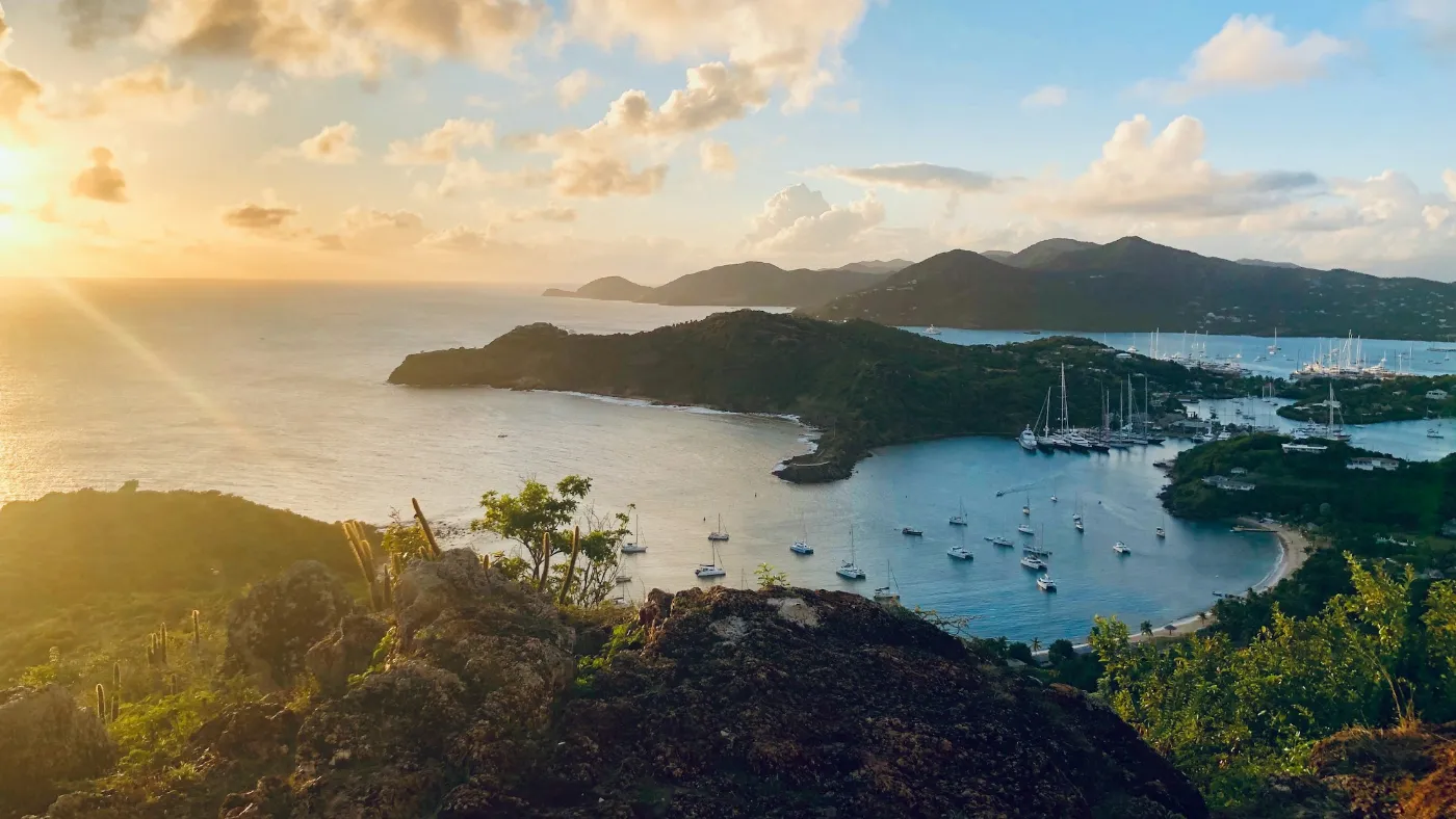 Yachts anchored in an Antigua harbour at golden hour, with green hills behind